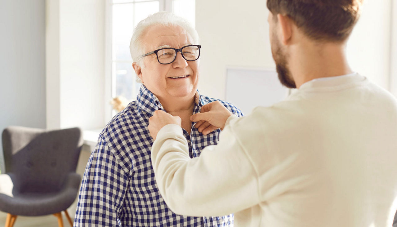 Adult son helping his senior father to button his shirt 