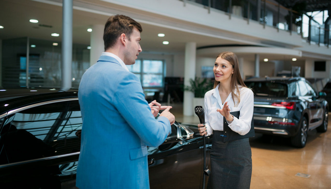 Female sales manager selling electric car to a male customer at showroom