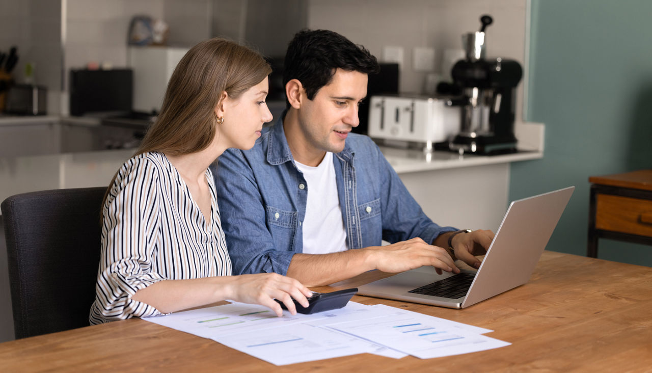 Young married couple in kitchen managing family budget on laptop