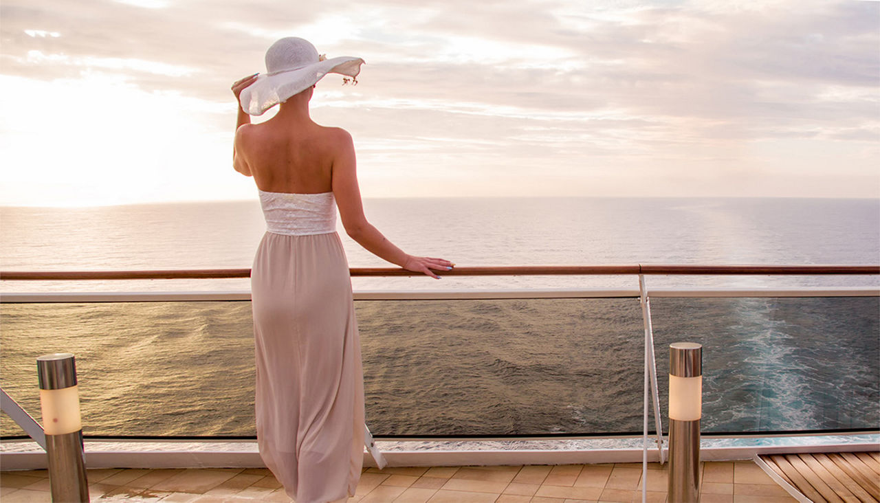 A woman in stylish cruise-wear looks out over the railing of a ship. 