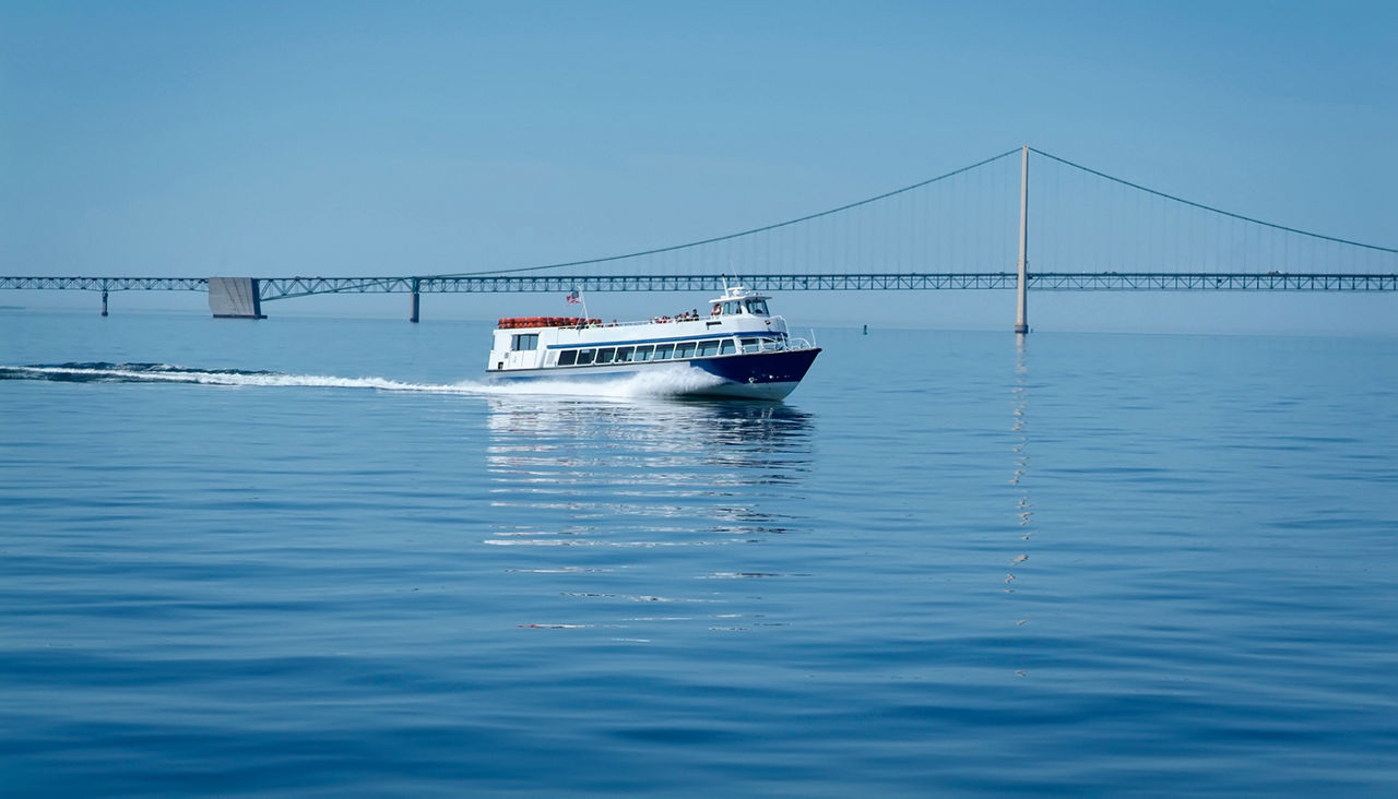 A passenger ferry boat crosses the Straits of Mackinac between Mackinac Island and Mackinaw City with the Mackinac bridge in the background.