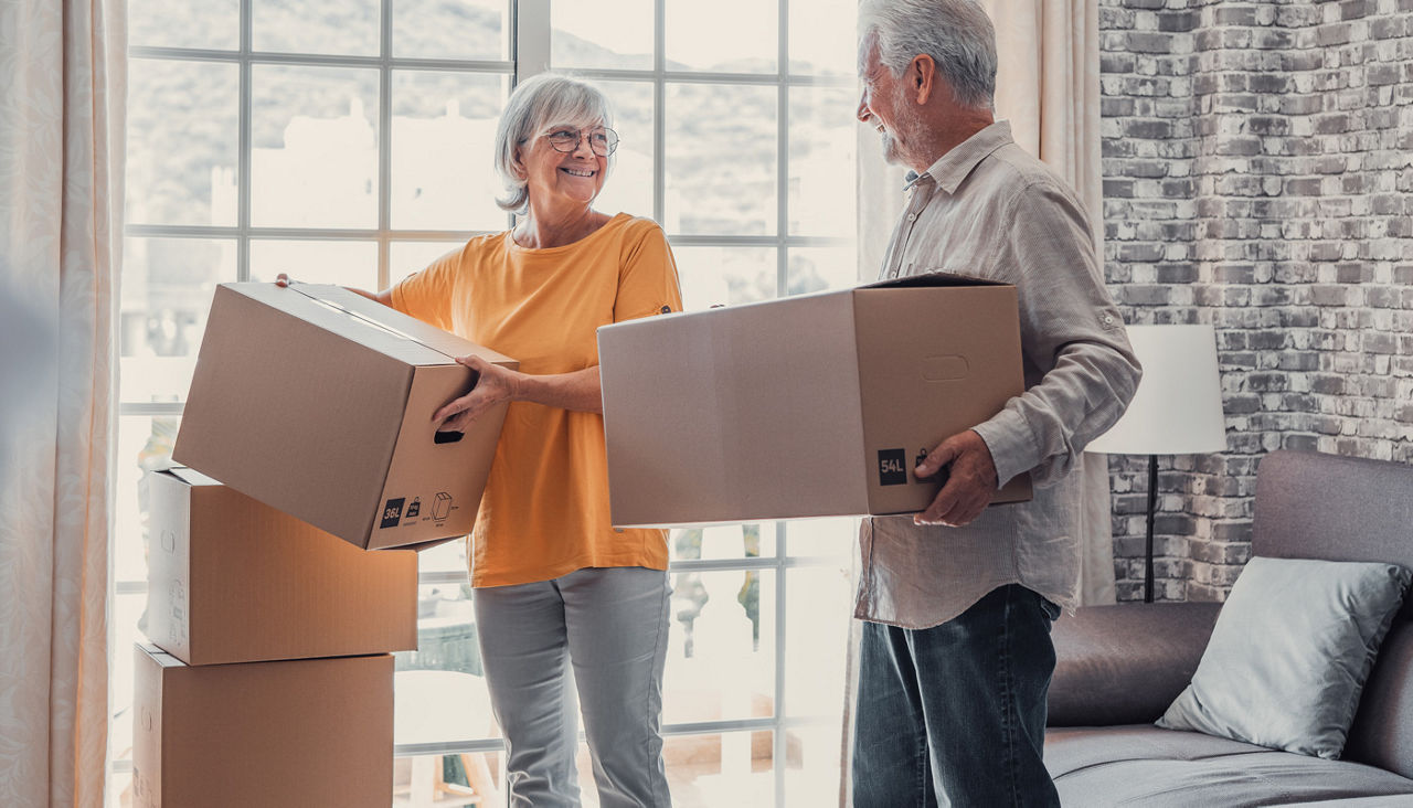 Mature couple moving into new apartment, carrying cardboard boxes into empty room