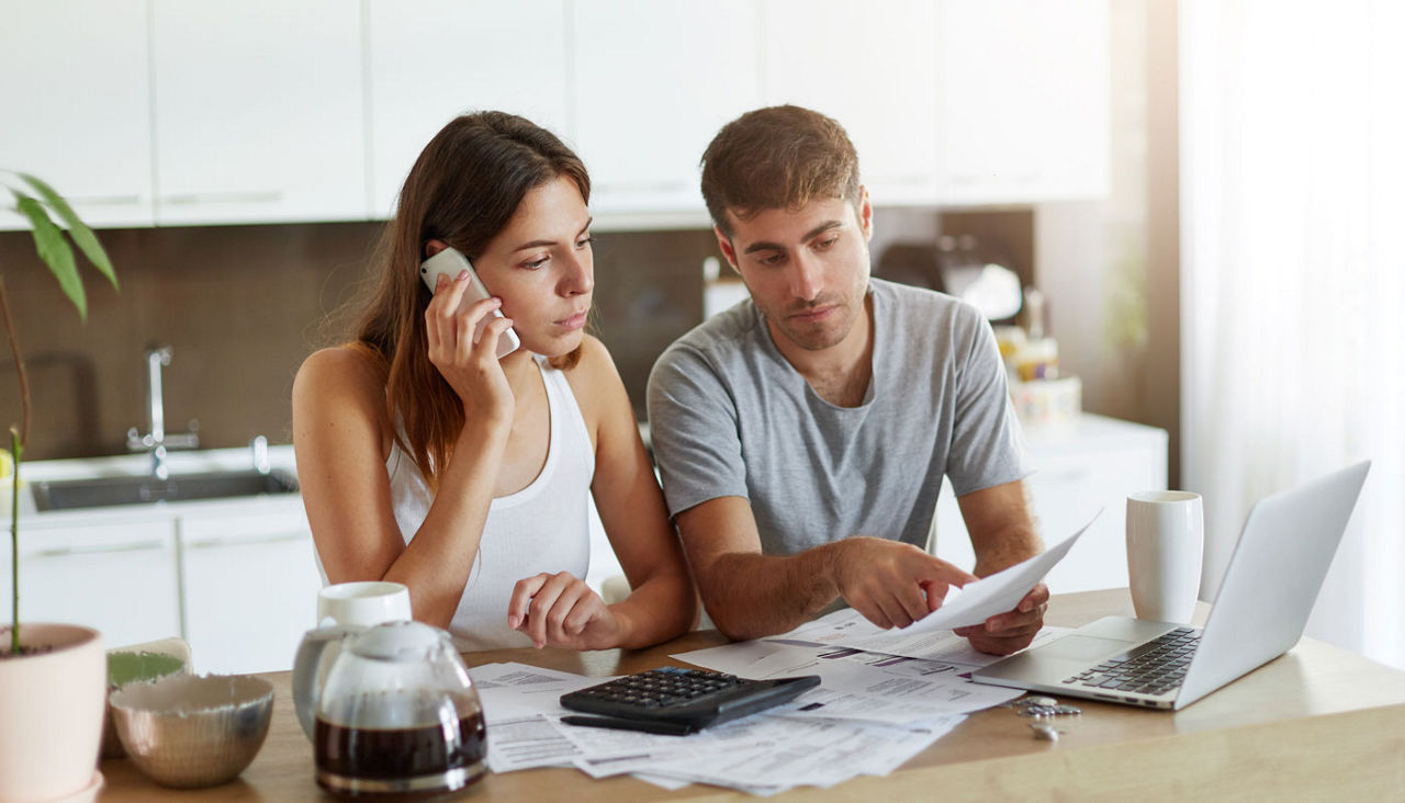Young couple at kitchen table reviewing finances with laptop and calculator