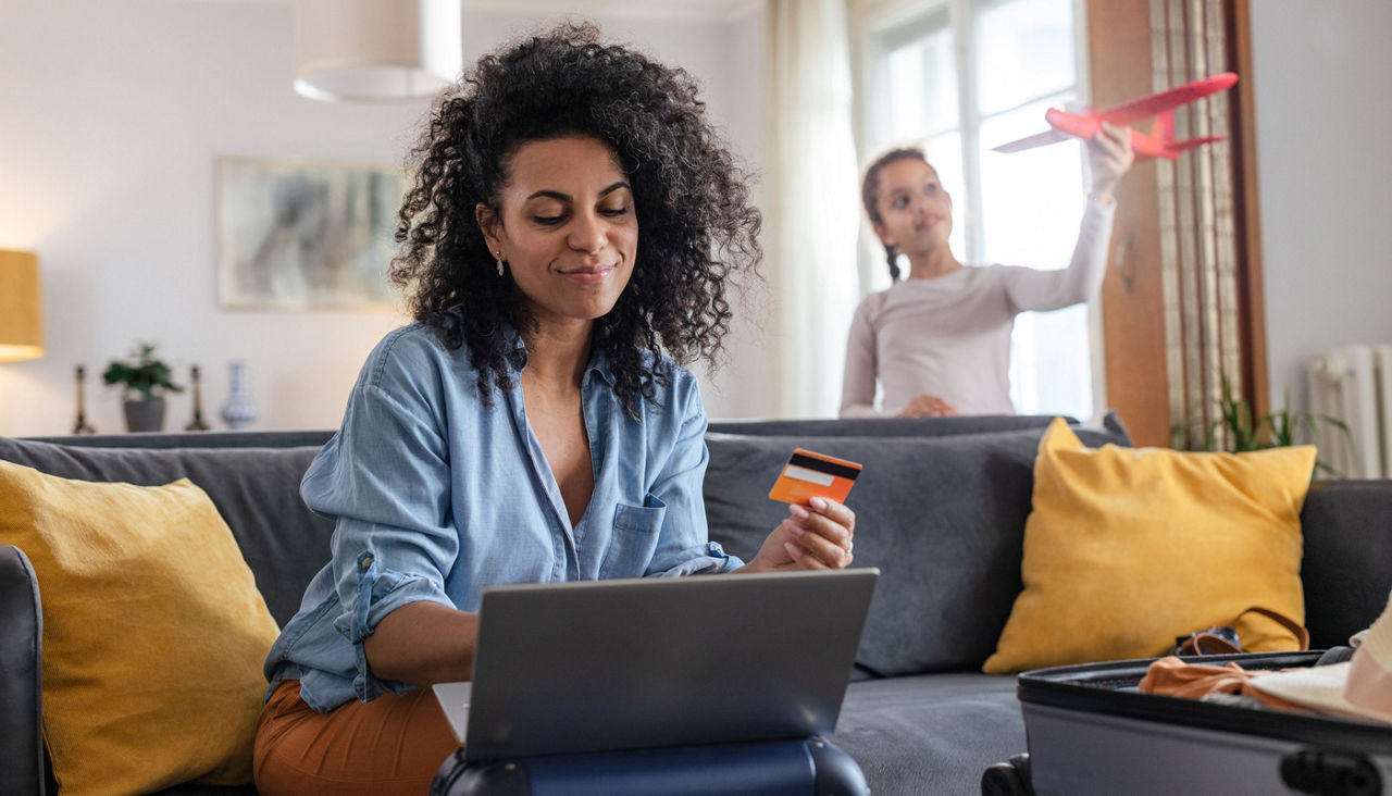 Woman is booking airplane tickets on her laptop as her teenage daughter plays joyfully with a toy airplane