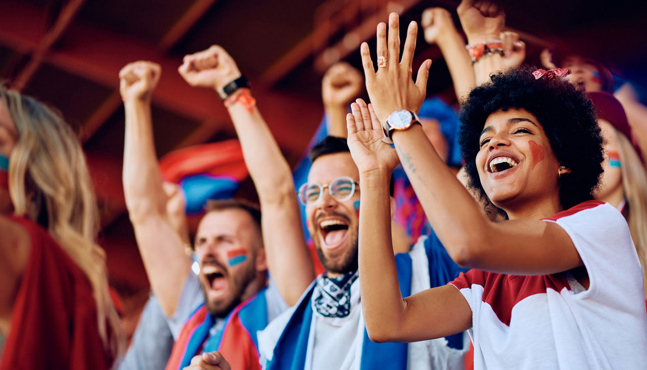 Group of cheerful sports fans celebrating victory of their favorite team while spectating game from stadium stands