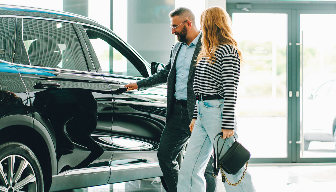 Car salesman showing a new car to a female customer in dealership