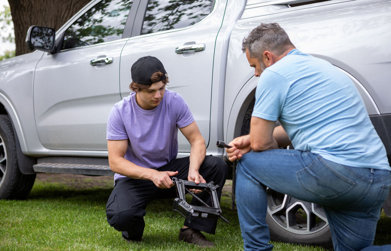 Father teaching his teenage son how to change a car tire 