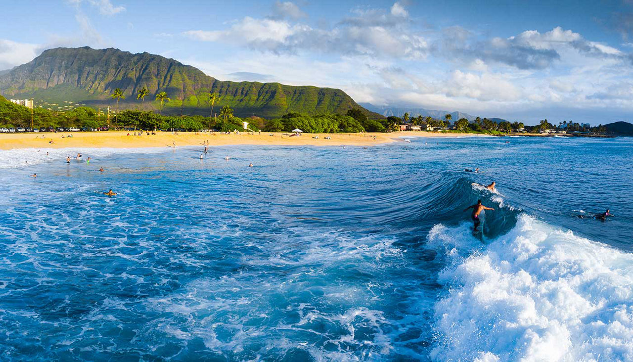 Panorama of surfers on wave with mountains in the back in Makaha