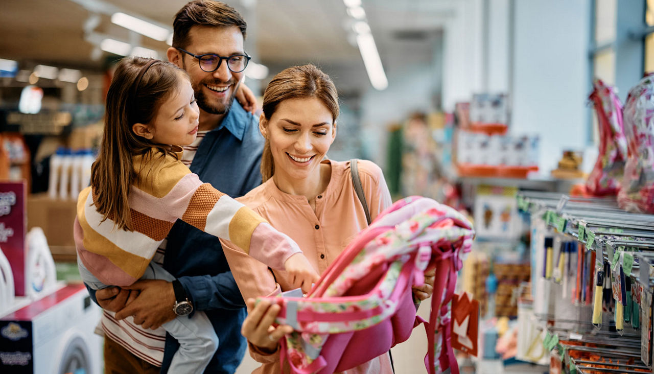 Little girl and her parents choosing backpack for school while shopping in store together.