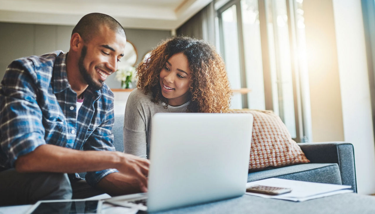 Couple working on laptop look happy and hopeful about their finances