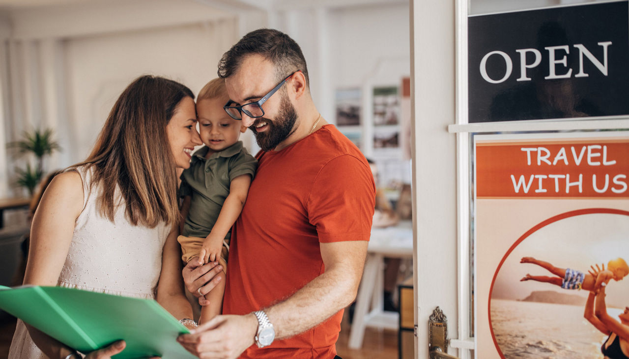 couple with baby son in modern travel agency looking where to go on vacation.