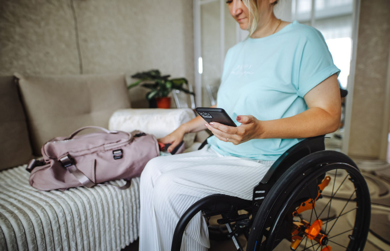woman in a wheelchair with a smartphone and a travel bag at home in the living room