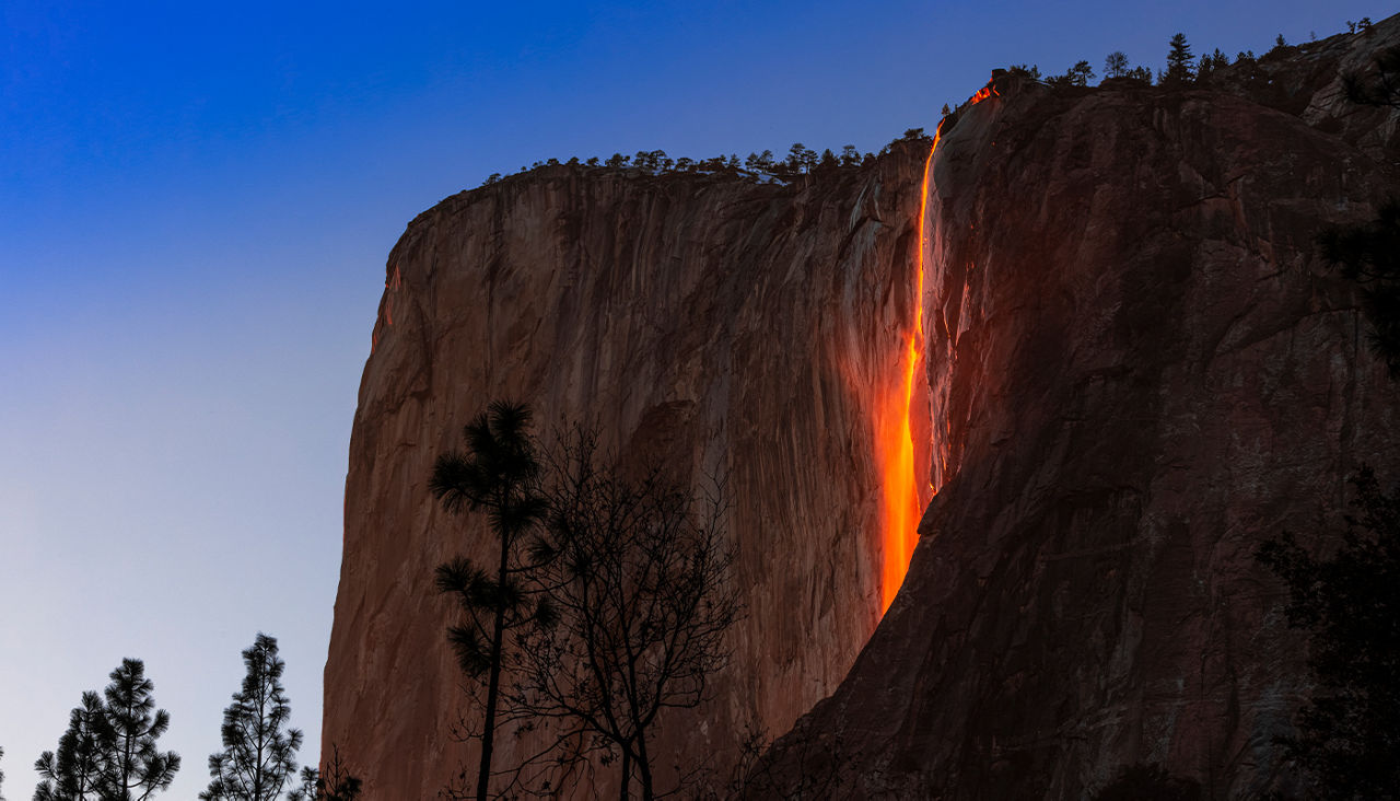 Waterfalls are tinted orange at sunset beside sequoia trees. 