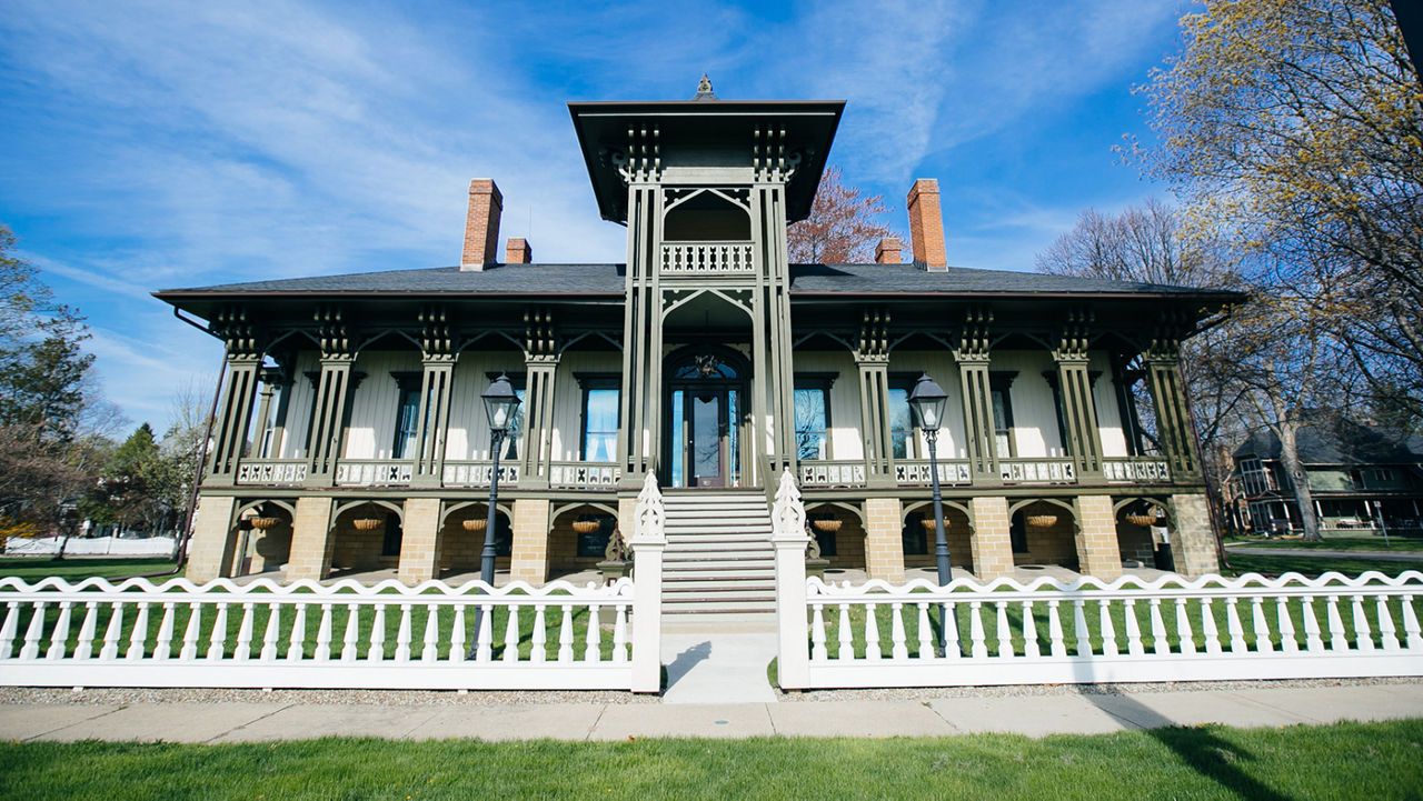 A Hawaiian-inspired historic house with green columns and a white fence in Marshall, Michigan