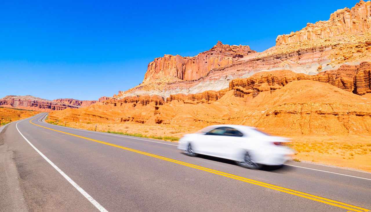 white car riding down road in canyon area
