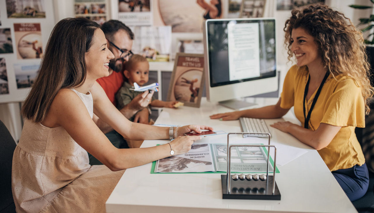 Married couple with baby son in modern travel agency talking to a woman