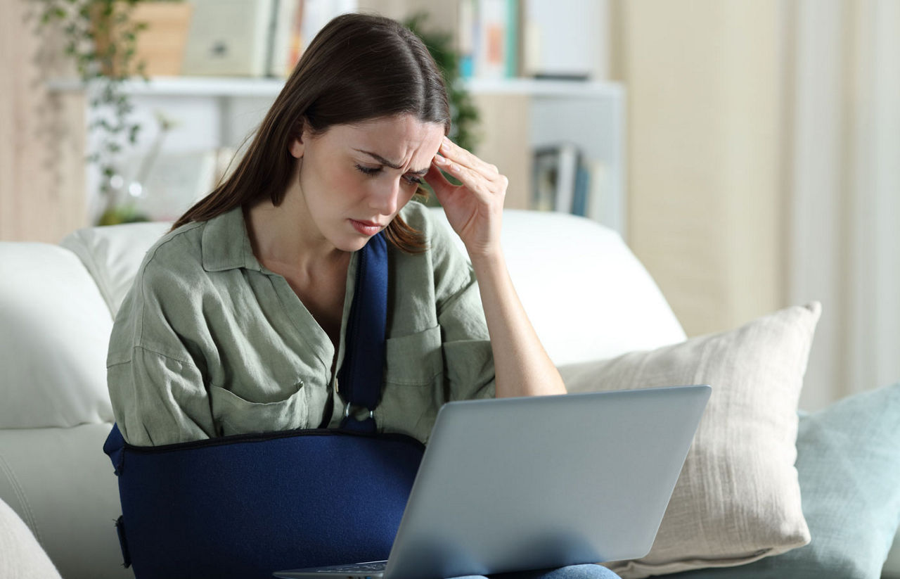 Worried woman with arm in sling looking at laptop