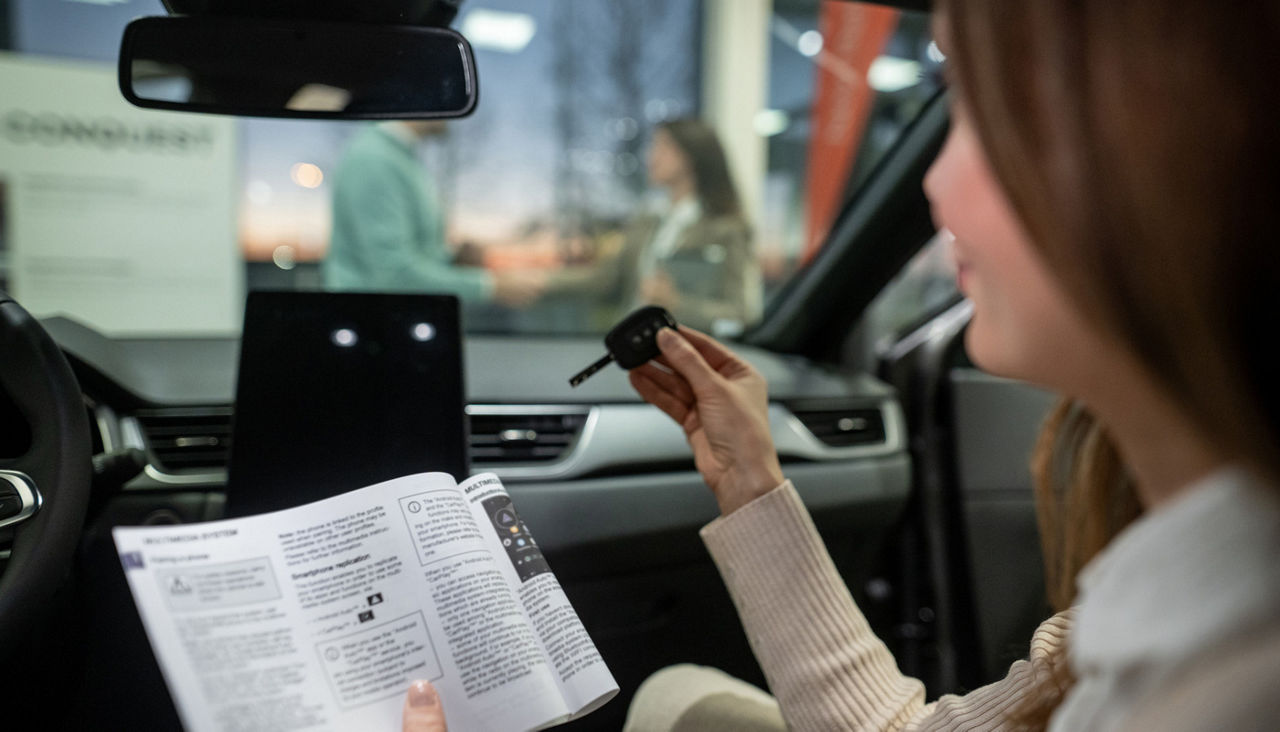 Woman holding car key and manual inside new vehicle