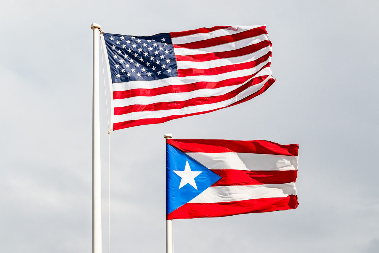 The American and Puerto Rican flags flying on a flag pole.