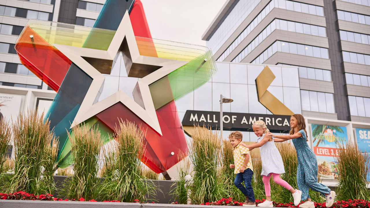 Kids in front of of a Mall of America sign with buildings in the background.