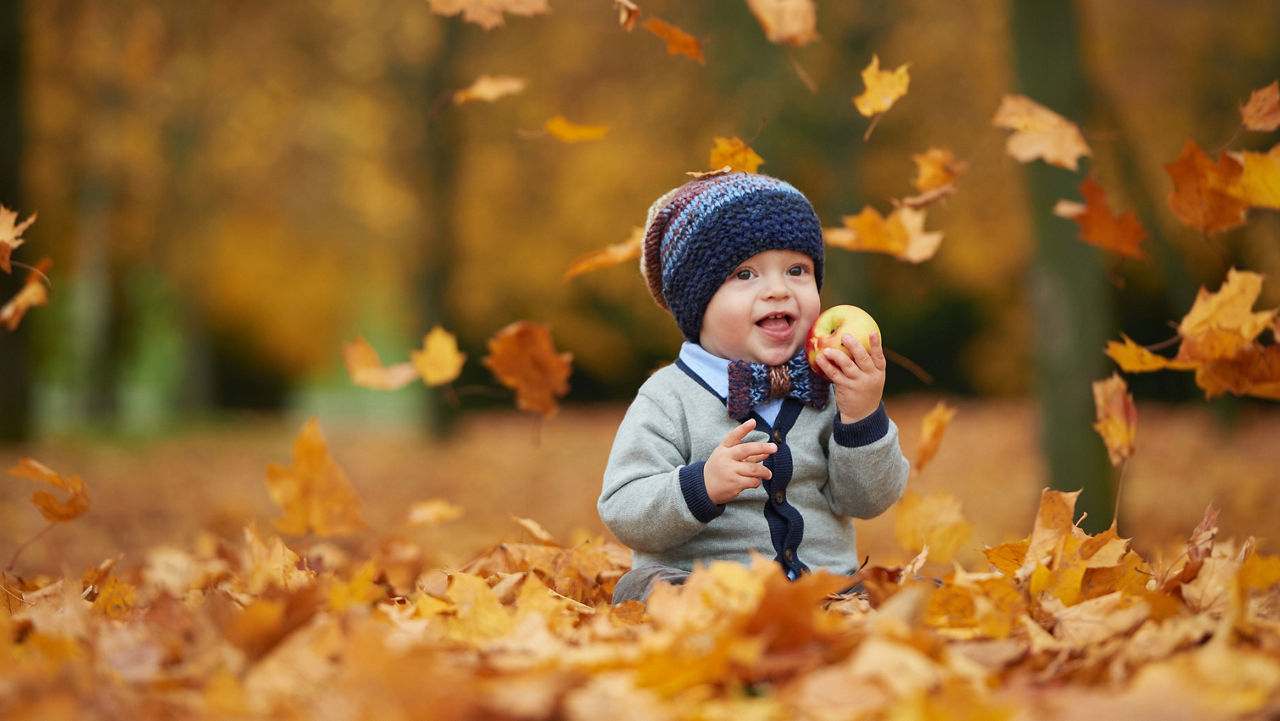 Baby in a leaf pile holding an apple.