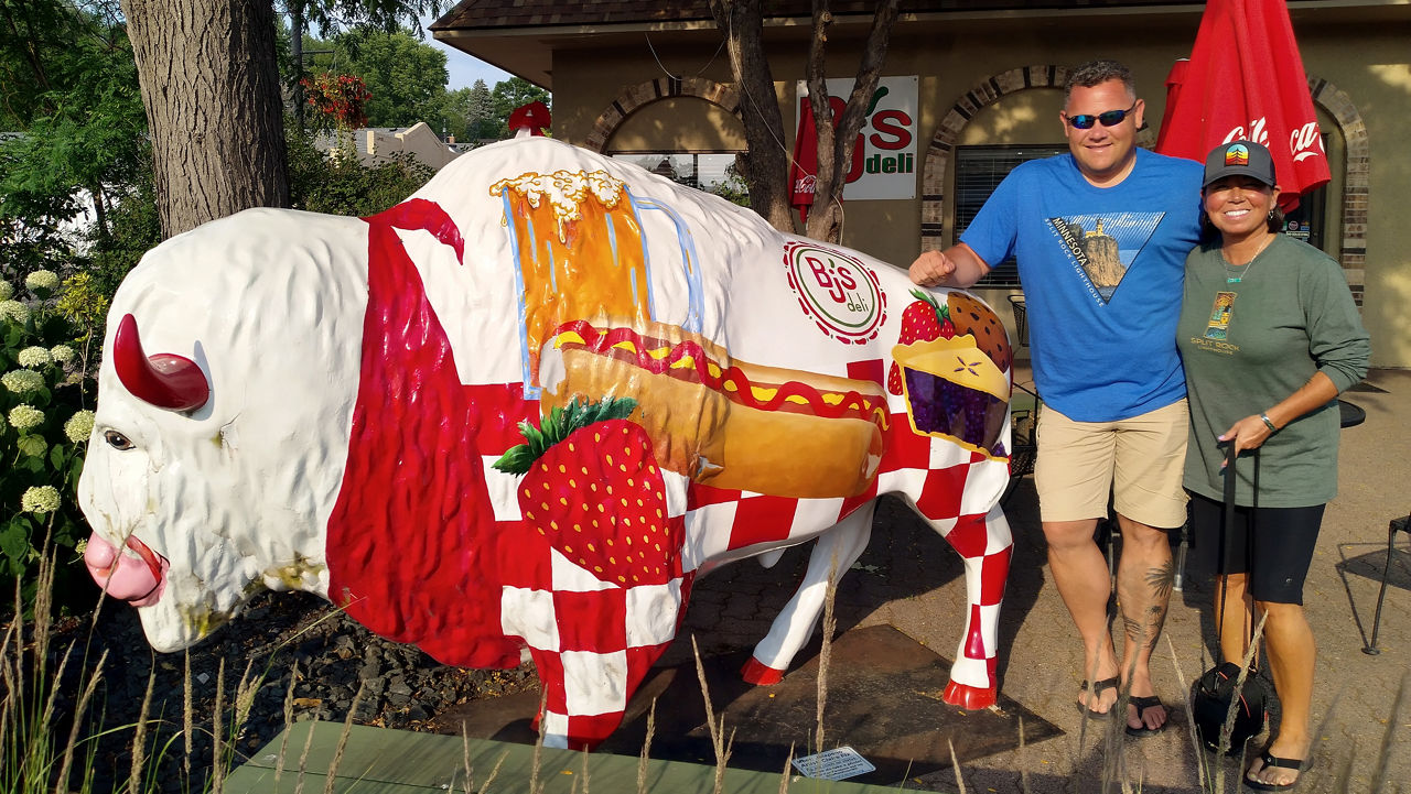 Buffalo statue painted with a red scarf, red and white checkers, a coney dog, strawberry, glass of beer, a slice of pie and the BJ's Deli logo.