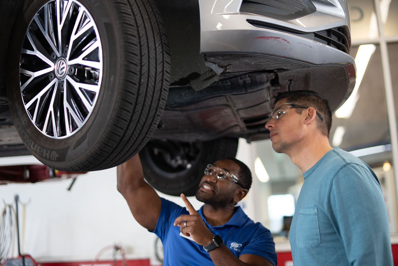 a mechanic showing off the bottom of a car to another man