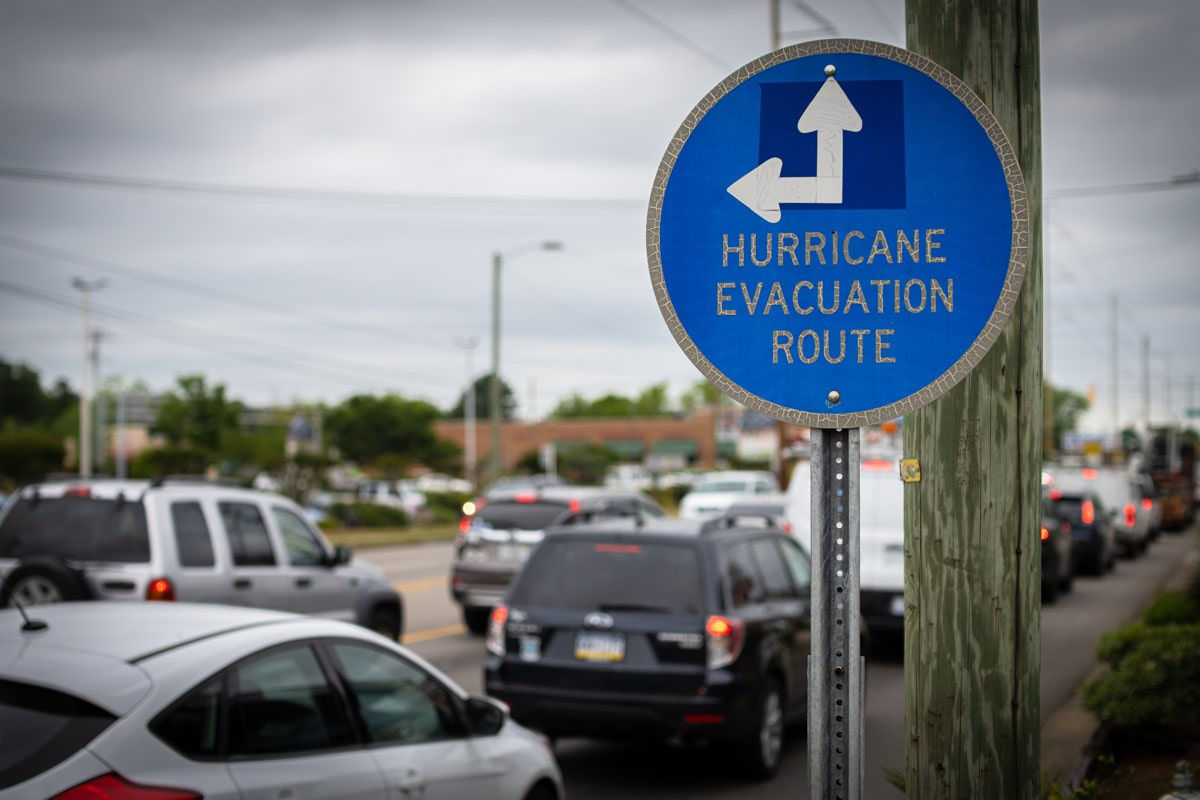 A blue hurricane evacuation sign with cars lined up on a roadway.