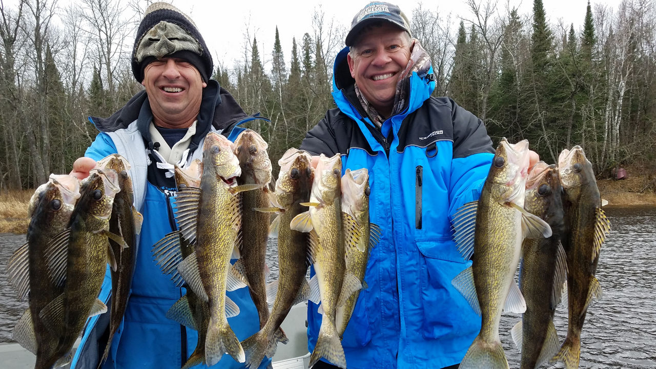 Two men in winter clothing holding up a string of fish with a river in the background.