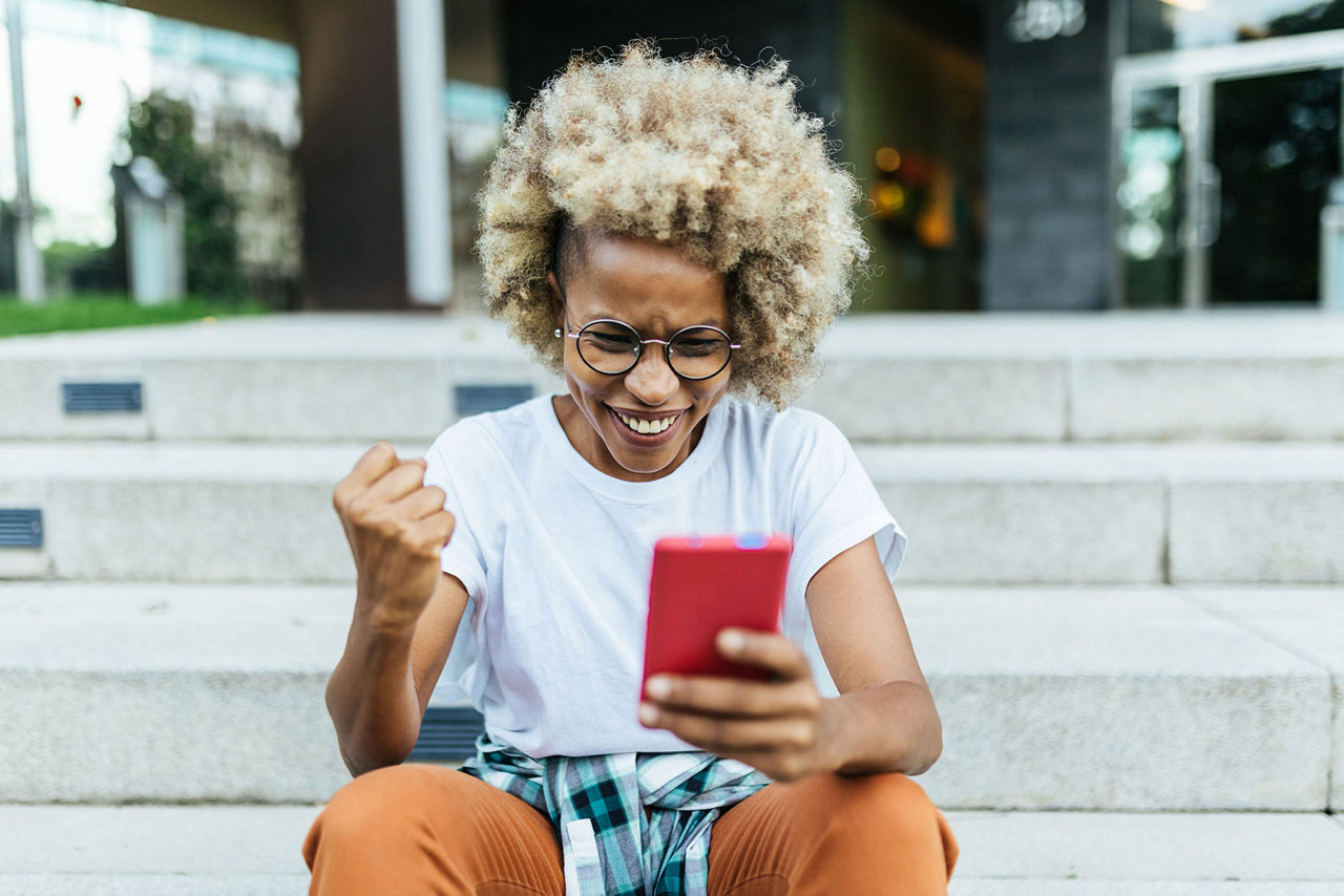 Excited mixed race young woman receiving good news on her mobile phone. Technology and success concept.