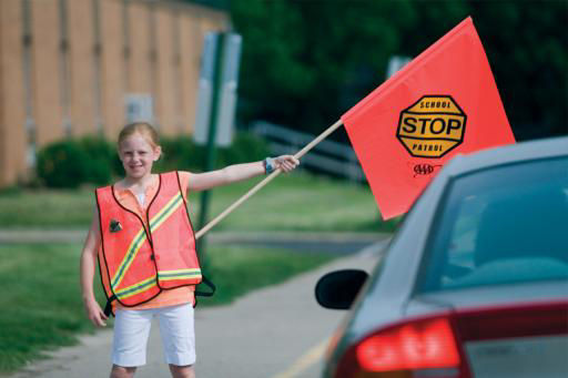 School Safety Patroller in crosswalk stopping a car with patrol flag