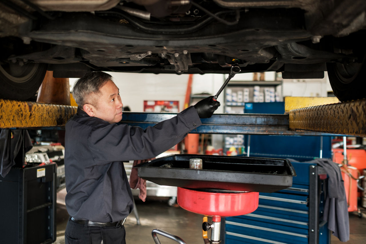 asian car mechanic performing an oil change in his auto repair