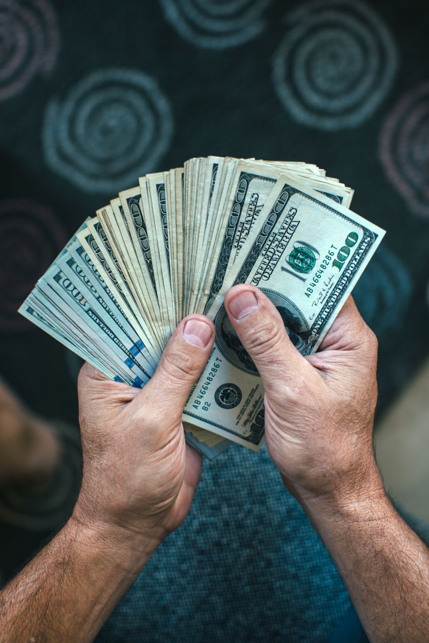 Man holding a large stack of fanned out hundred dollar bills