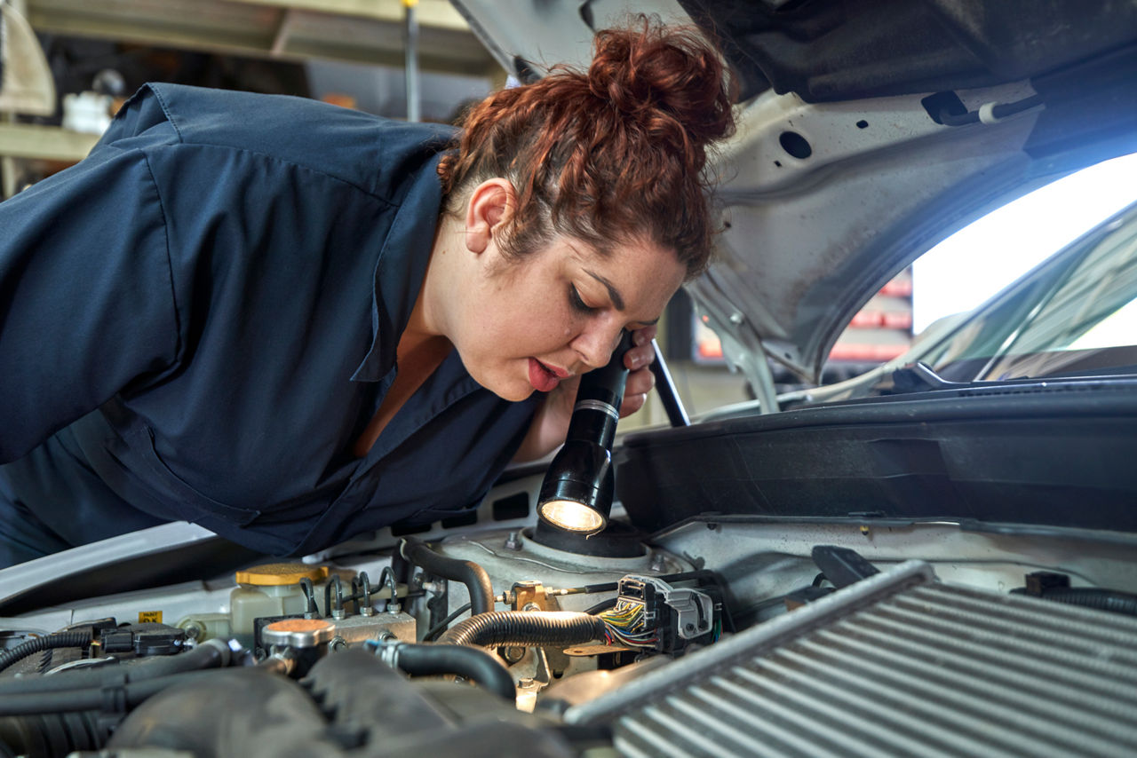 Mechanic looking into the engine of a car with a flashlight.