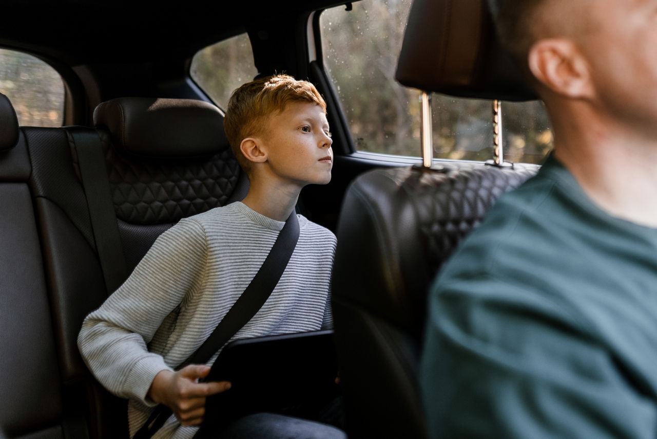 child looking outside his car door window as his father is driving.
