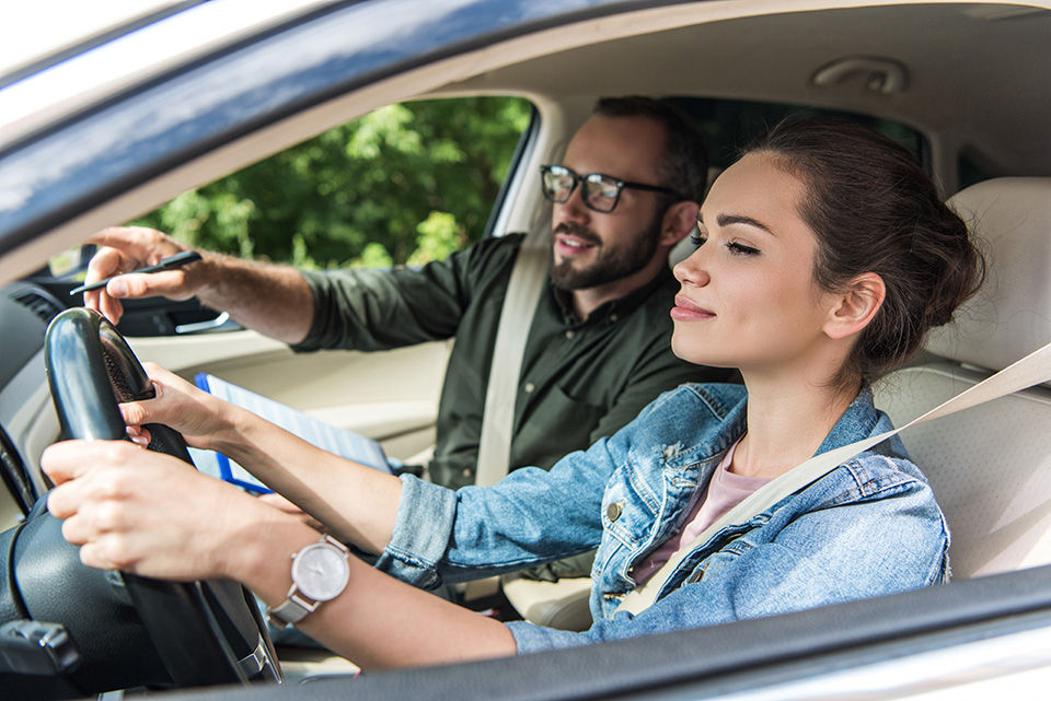 Driving instructor inside a car with a cheerful student during her driving test.