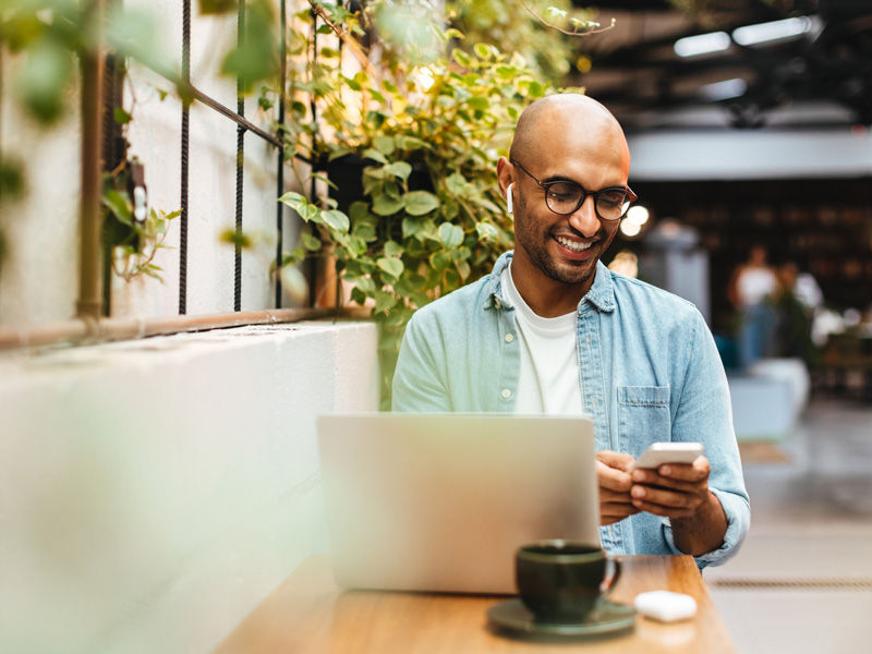 Man reading content on his phone and laptop in an outdoor atmosphere