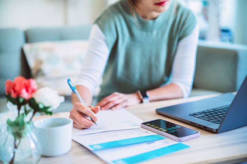 A woman taking notes from something she is watching on her computer.
