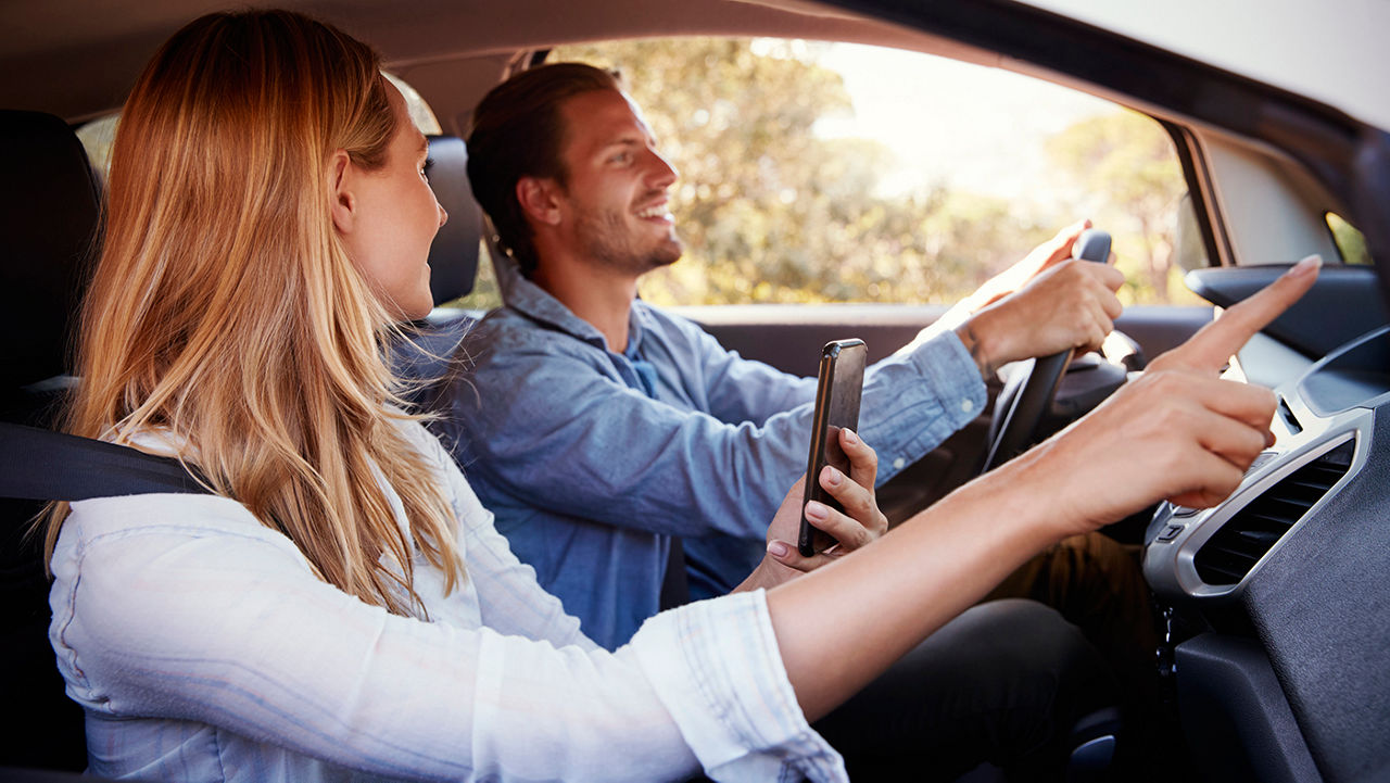 Young couple in car using smartphone to navigate their trip
