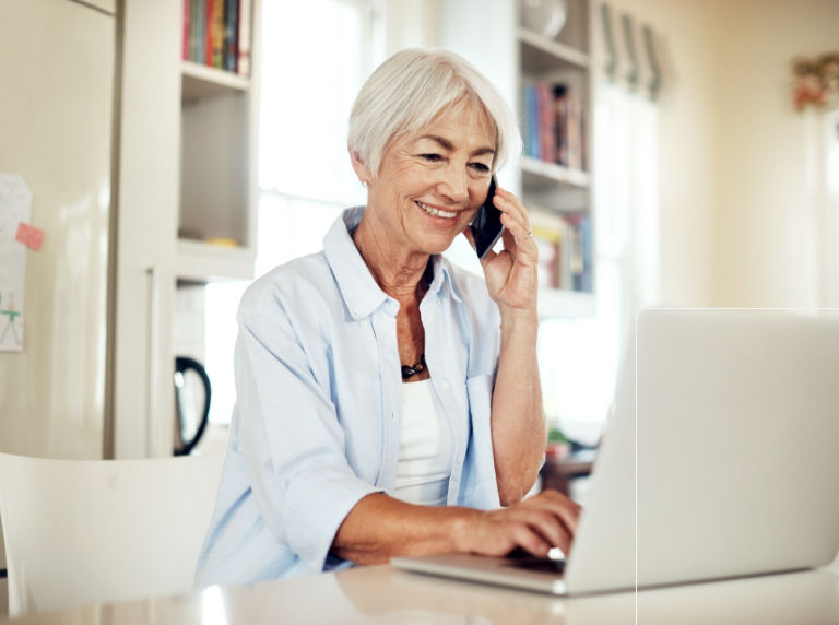 Woman smiling while talking on the phone looking at her laptop. 