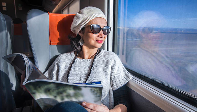 Woman seated in a train car wearing sunglasses and looking out the window.