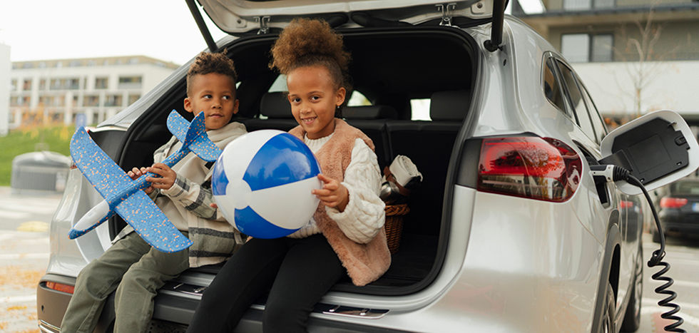 Cheerful kids sitting in car trunk and waiting for car charging.