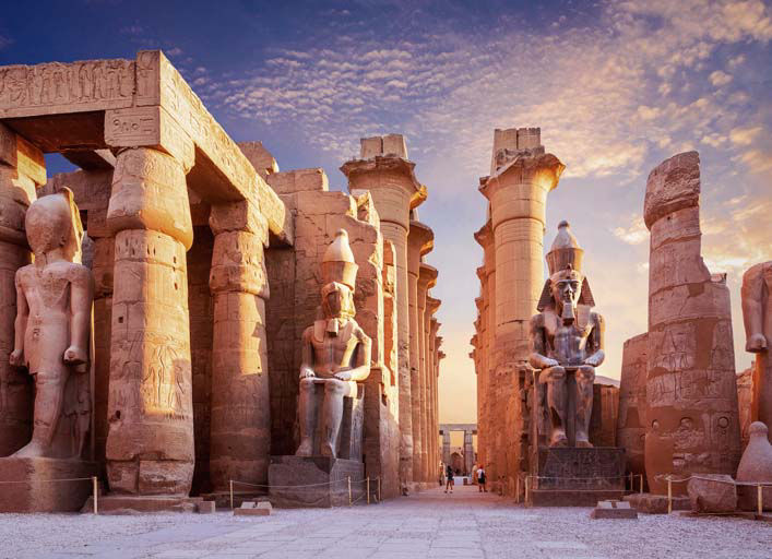 Ancient statues and towering columns of Luxor Temple glowing in the warm sunset light.