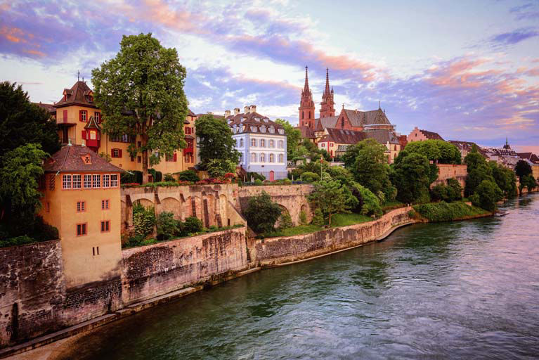 Colorful historic buildings along the Rhine River at sunset in Basel.