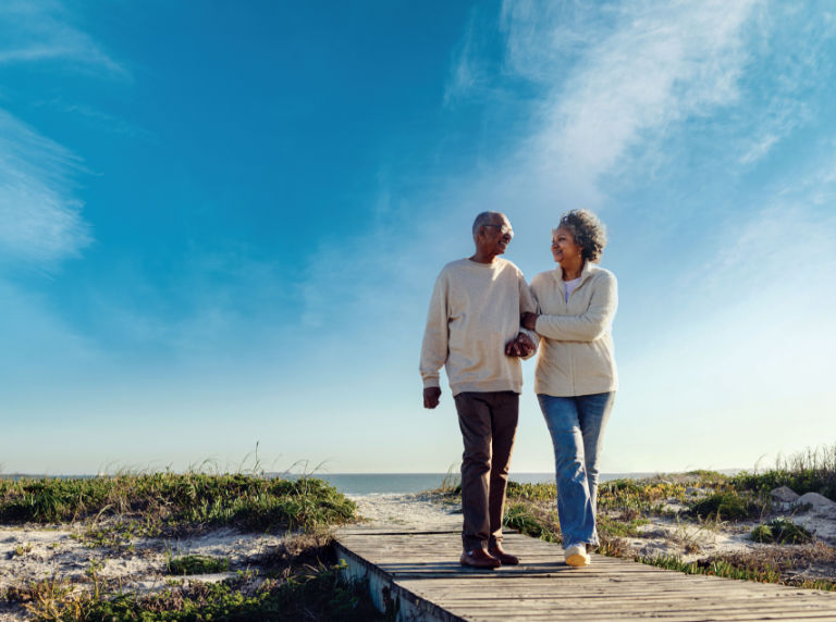 Couple walking arm in arm down the boardwalk at the beach.