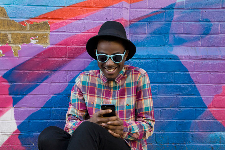 Man in hat using AAA app on his smart phone near a colorful wall.