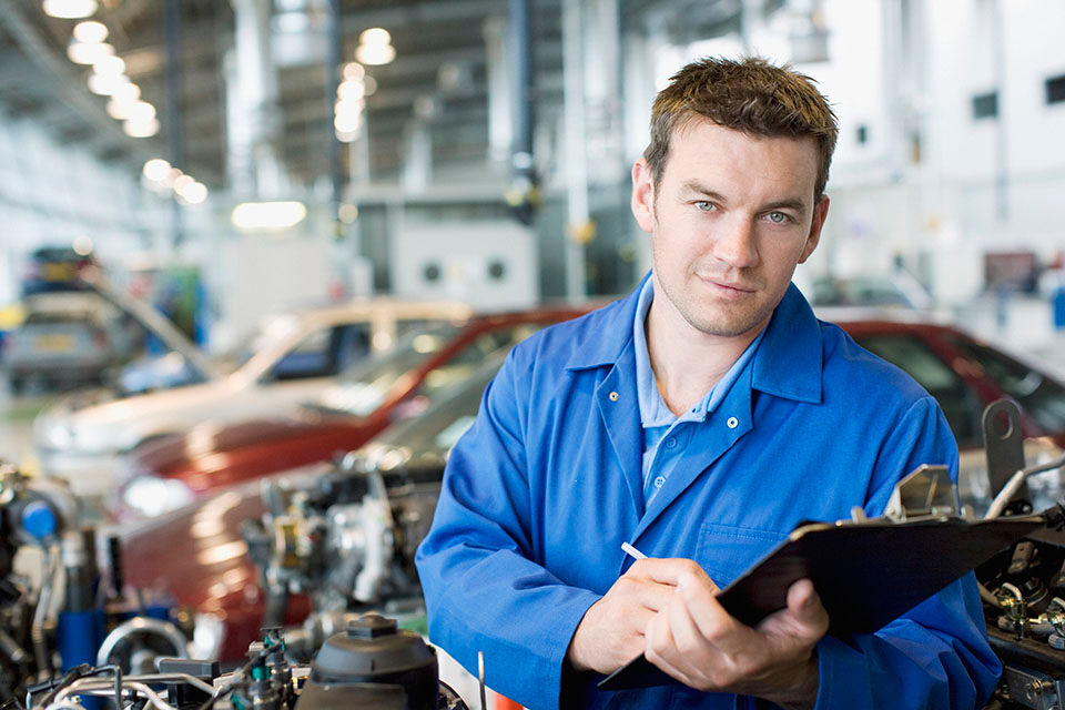 Mechanic holding a notepad next to a car that is being fixed.