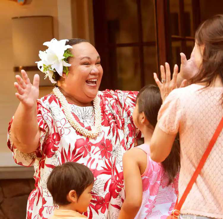 Auntie welcomes the children in a hawaiin patterned dress with open arms.