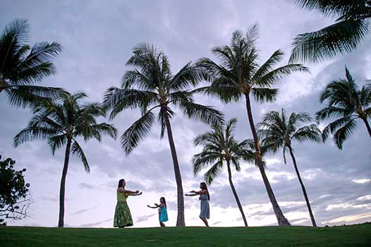 Women is teaching two little girls hula at sunset.