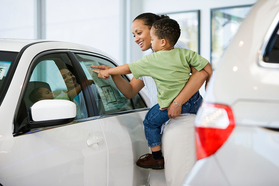 Woman holding son while looking at a car to buy. 